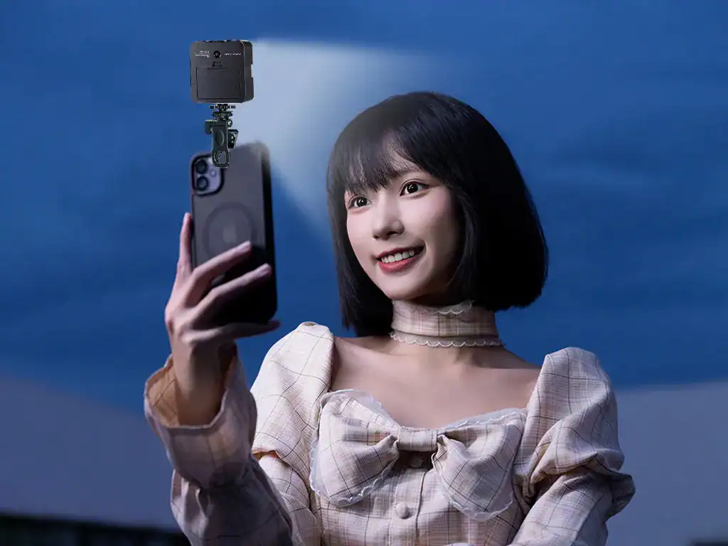 Fotografia de uma jovem sorridente usando um vestido xadrez puxando um celular com câmera em um cenário ao entardecer, demonstrando tecnologia e inovação.