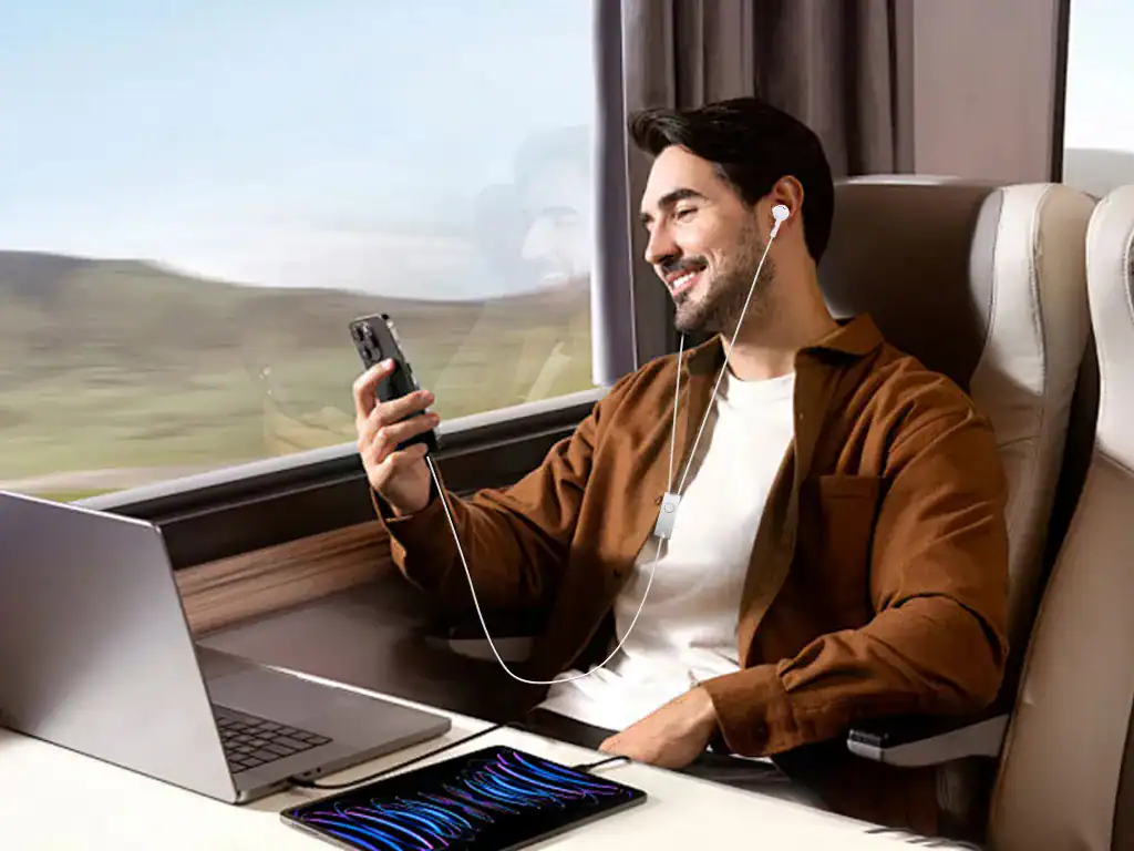 Conforto e tecnologia na viagem: homem sorridente usando fones de ouvido, celular e laptop em trem moderno, aproveitando momentos de lazer e trabalho durante a viagem.