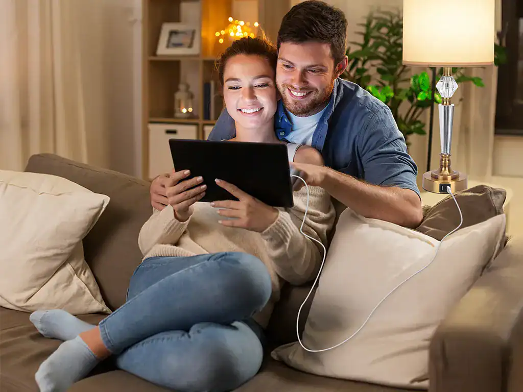 Conforto na sala decorada com luzes suaves, casal assistindo TV e usando tablet, ambiente acolhedor com iluminação quente, ideal para momentos de lazer em casa.
