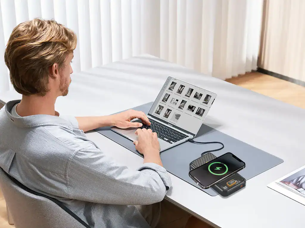 Carregador wireless para smartphones em uso no escritório, com laptop e revista na mesa de trabalho.