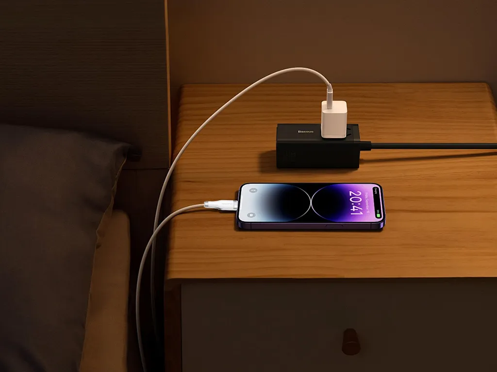 Carregador de celular conectado a uma tomada na mesa de cabeceira com o smartphone carregando, evidenciando comodidade e tecnologia para uso diário.