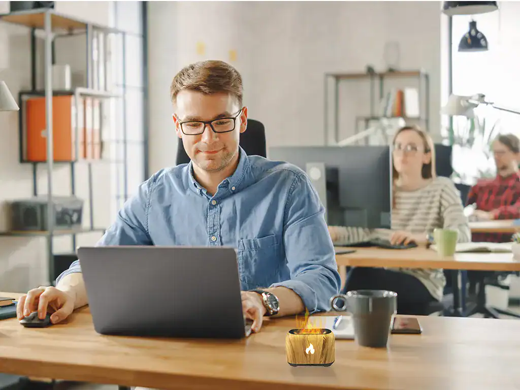 Homem usando laptop em ambiente de escritório com colaboradores ao fundo, refletindo modernidade, inovação e tecnologia.