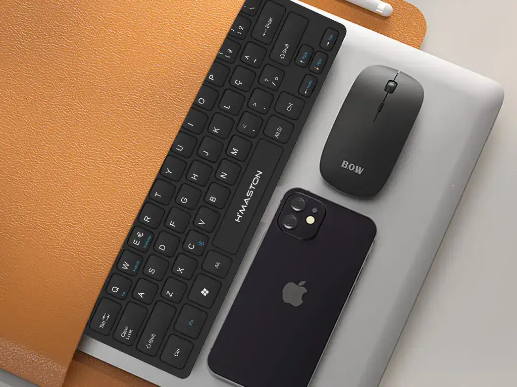 Teclado e mouse sem fio compatíveis com computadores e dispositivos móveis, acompanhados de um smartphone e um laptop, ideais para trabalho remoto e produtividade.