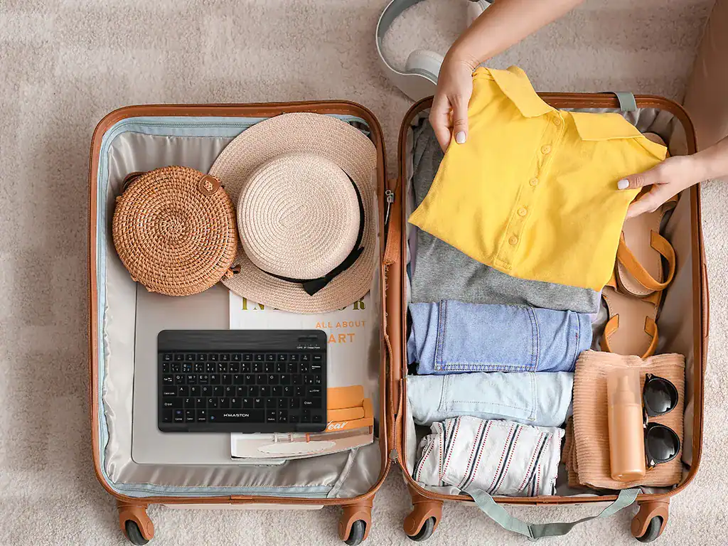 Malas abertas com roupas, chapéus, óculos de sol e itens de viagem organizados.