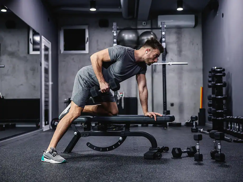 Homem realizando exercício de força com peso em academia moderna.
